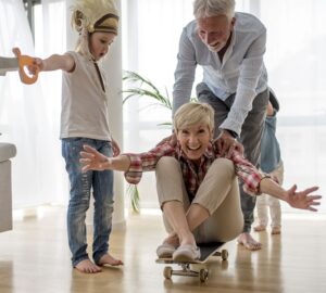 Caucasian grandfather pushing grandmother on skateboard inside with grandson wearing pirate costume