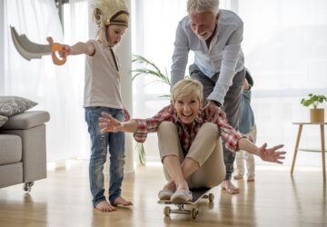 Caucasian grandfather pushing grandmother on skateboard inside with grandson wearing pirate costume