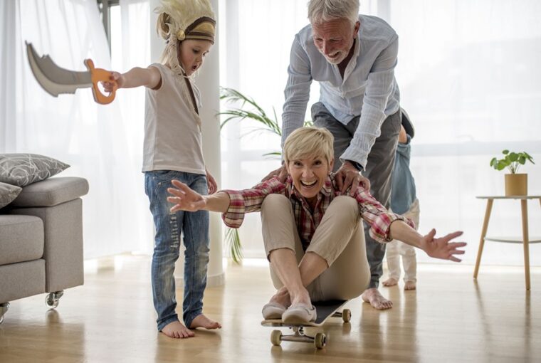 Caucasian grandfather pushing grandmother on skateboard inside with grandson wearing pirate costume