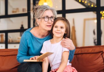 Nice elderly woman grandmother reading story to granddaughter.